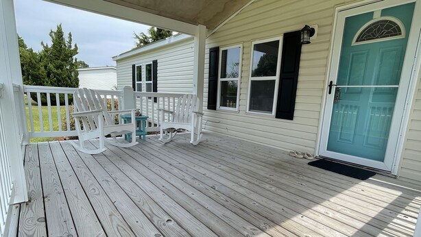 A covered wooden deck with white chairs and a door with a glass panel.