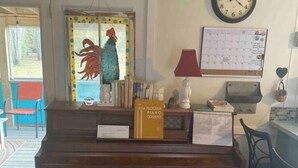 A living room with a wooden piano, a wall clock, a calendar, and a rooster decoration.