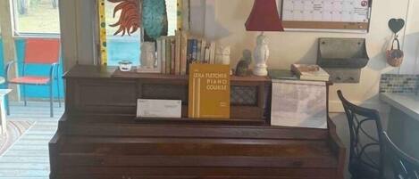 A living room with a wooden piano, a wall clock, a calendar, and a rooster decoration.