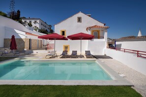 A swimming pool with lounge chairs and umbrellas, a white building with yellow accents, and a clear blue sky. - Casa Lidador (Obidos)