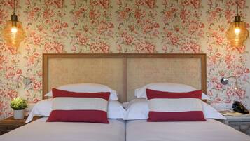 Una cama doble con ropa de cama blanca y roja, un cabecero de madera y papel tapiz con motivos florales.