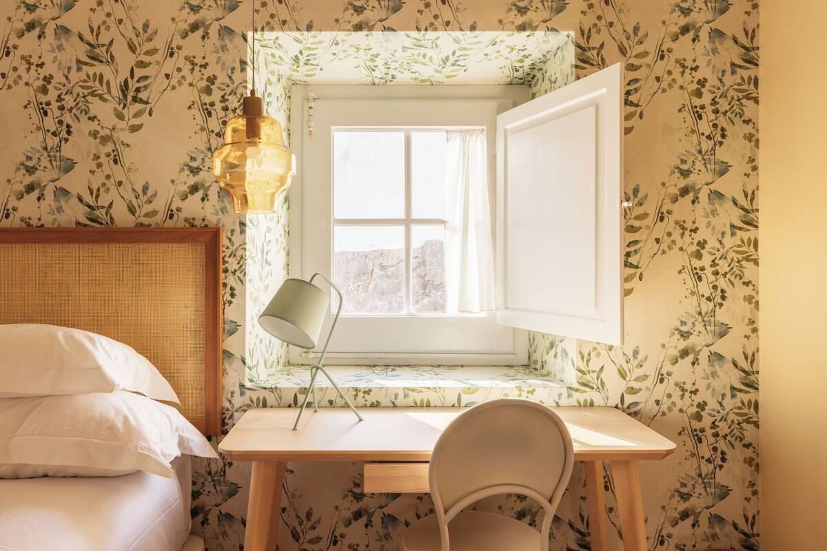 A bedroom with a bed, a desk with a chair, a window with curtains, and a hanging lamp.