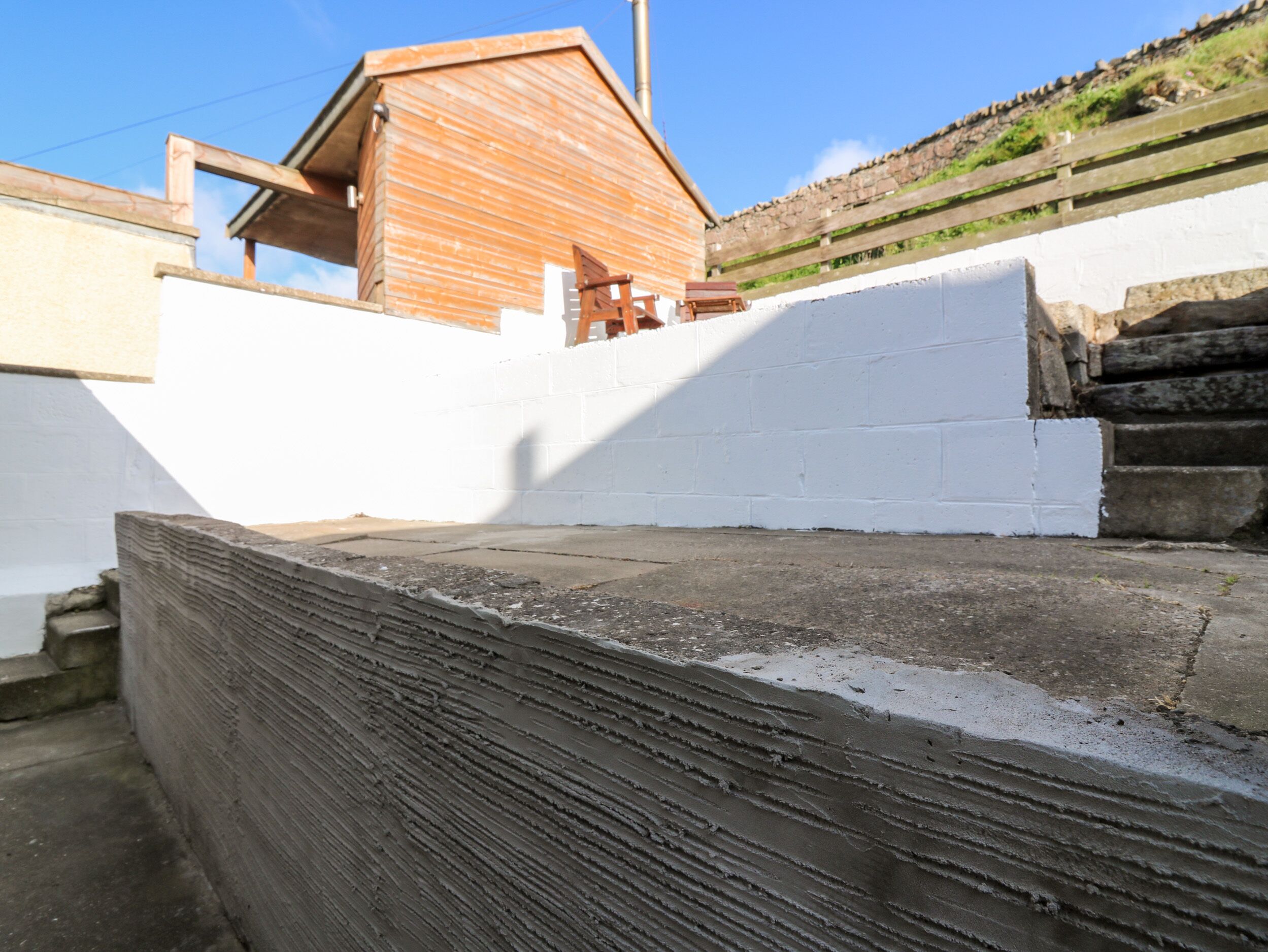 A wooden cabin with a sloped roof, white walls, and a stone foundation.