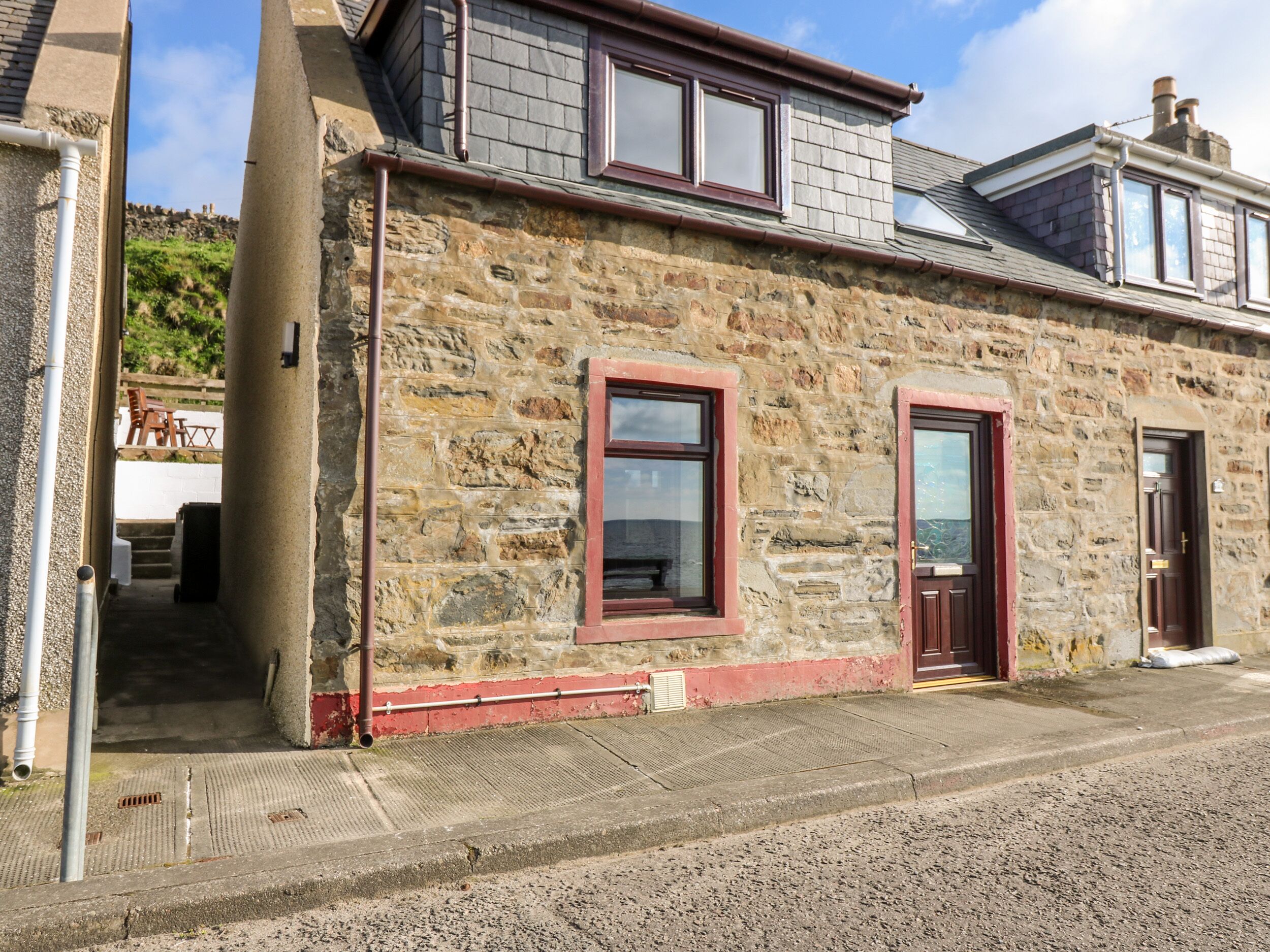 A stone building with a red door and windows, a small porch, and a view of the surrounding area.