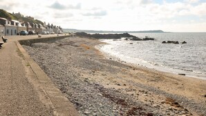 A pebble beach with a promenade, rocky shoreline, and buildings along the coast. - Dolphin Cottage (Banff)