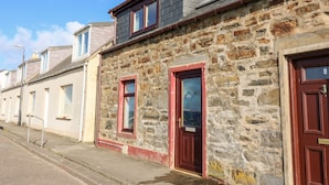 A row of stone buildings with red doors and windows, a clear sky, and a street in front. - Dolphin Cottage (Banff)