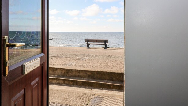 A wooden door with a metal handle, a bench on a sandy beach, and a view of the ocean. - Dolphin Cottage (Banff)