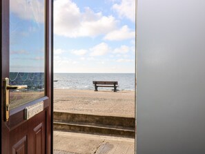 A wooden door with a metal handle, a bench on a sandy beach, and a view of the ocean.