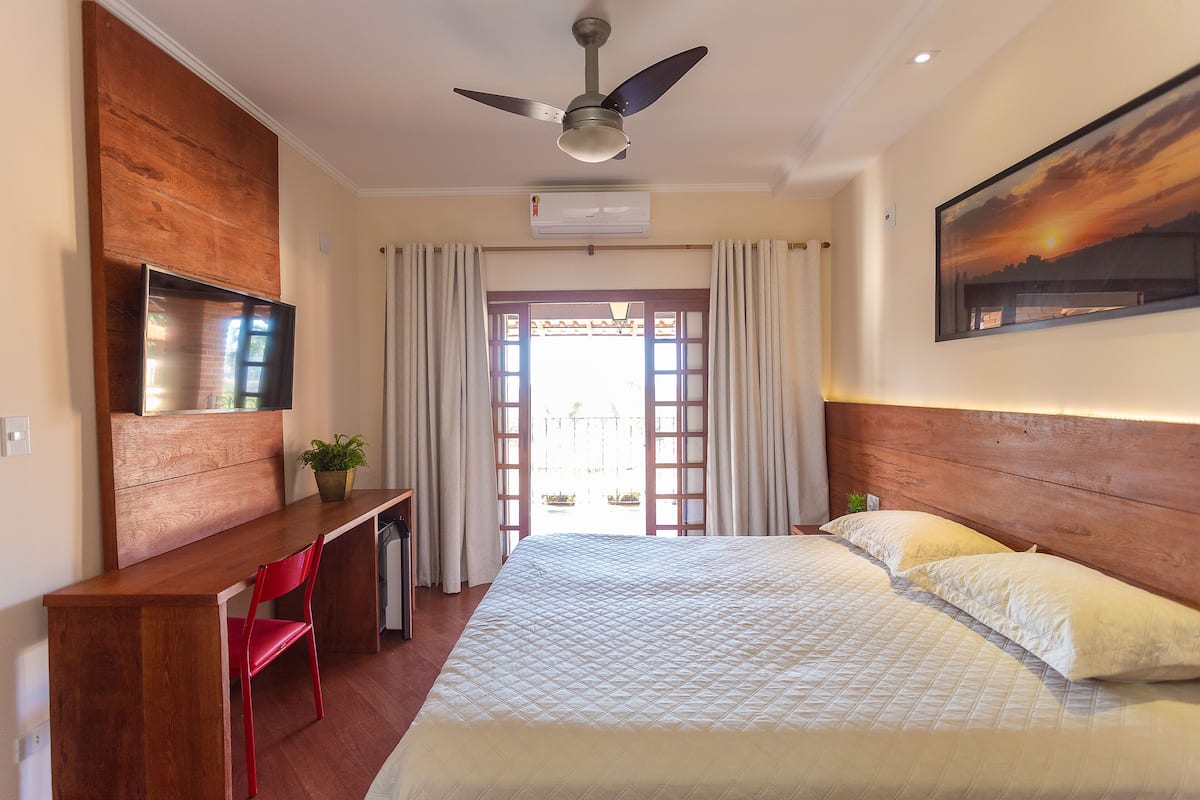 Ein Hotelzimmer mit Bett, Schreibtisch, Stuhl, Deckenventilator, Klimaanlage und einem Vorhangfenster.