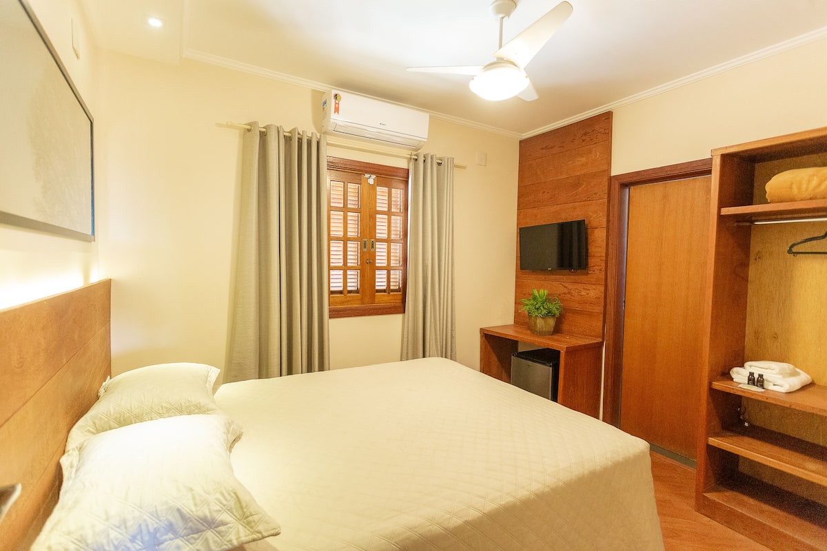 Ein Hotelzimmer mit Bett, Schreibtisch mit Pflanze, Kleiderschrank und Deckenventilator.