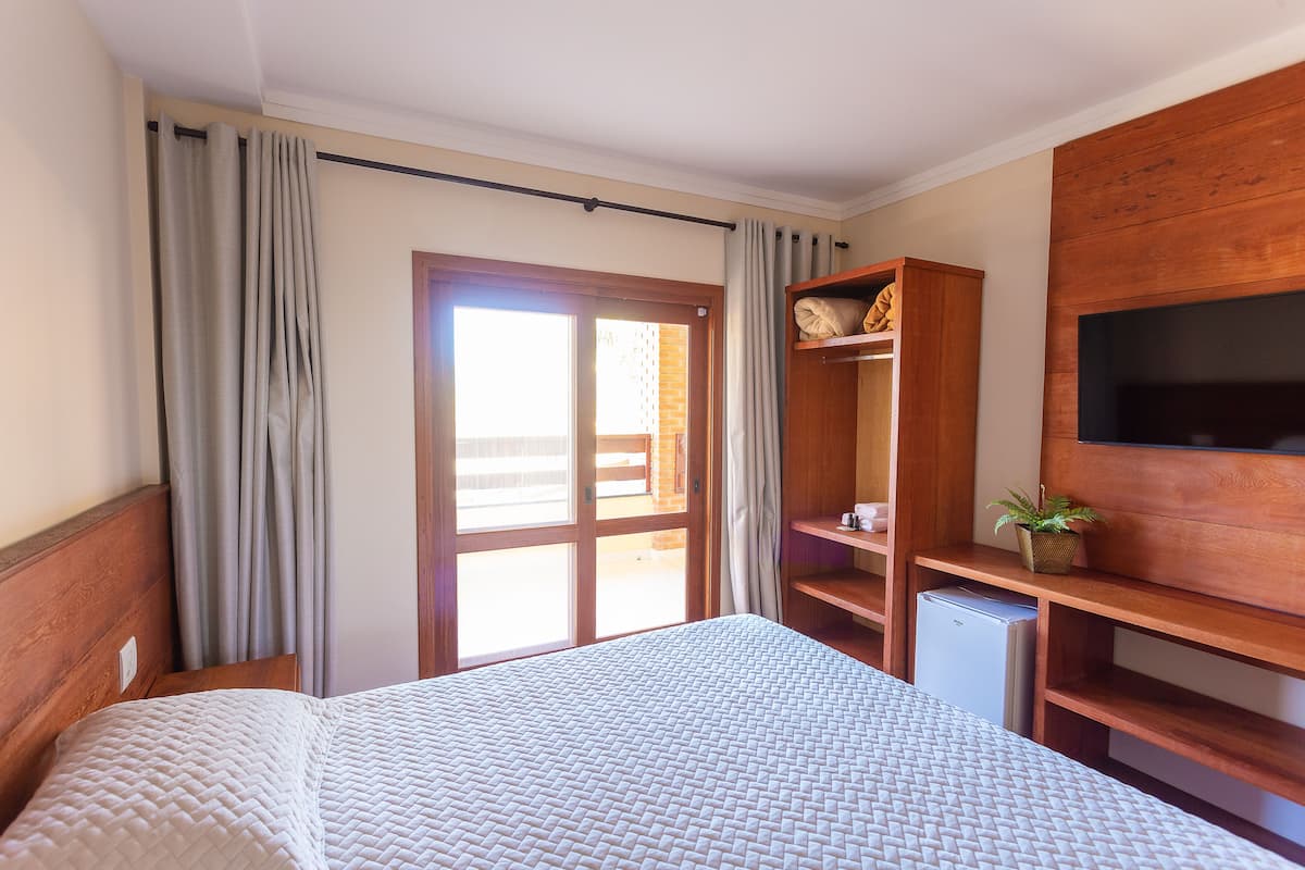 Ein Hotelzimmer mit einem Bett, einem an der Wand befestigten Fernseher, einem Holztisch und einem kleinen Kühlschrank.