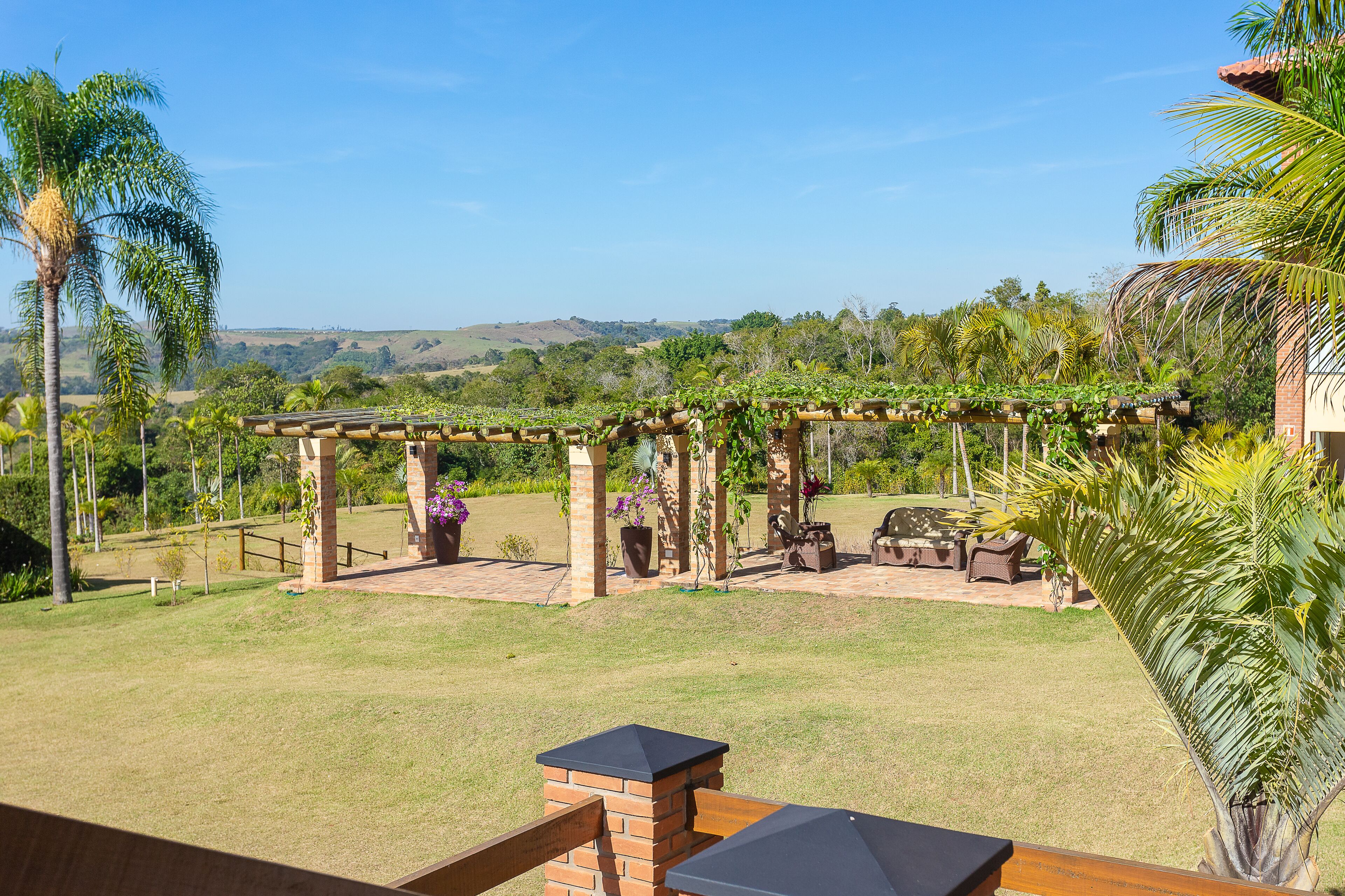 Uma área de pátio com pérgola, mobiliário externo e vista para a paisagem ao redor.