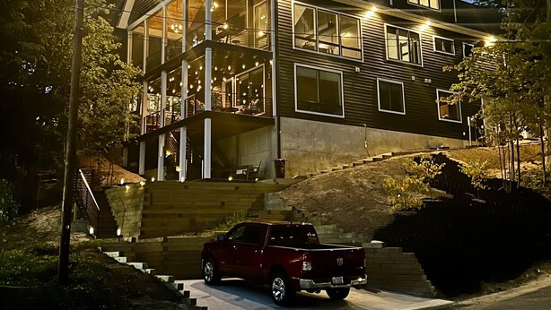 A modern two-story house with a balcony, a staircase leading to the entrance, and a red pickup truck parked in front. - Modern, Chic Adult ONLY Retreat On Hill w/Sunset Views Steps from Downtown  (Saugatuck)