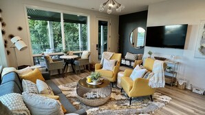 A modern living room with a sofa, armchairs, a coffee table, and a TV. There is a large window providing a view of the outdoors. - Modern, Chic Adult ONLY Retreat On Hill w/Sunset Views Steps from Downtown  (Saugatuck)