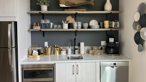 A modern kitchen with a stainless steel refrigerator, a Bosch dishwasher, and a microwave. There are two shelves above the sink with various kitchen items and a decorative fish sculpture. - Modern, Chic Adult ONLY Retreat On Hill w/Sunset Views Steps from Downtown  (Saugatuck)