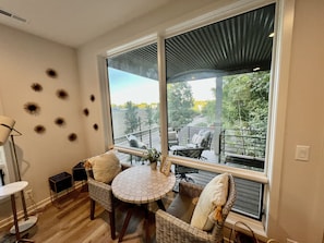 Relax in this serene space with a large window offering a view of the deck area, complete with a round table and wicker chairs.