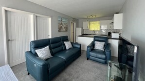 Een woonkamer met een bank, fauteuils, een glazen salontafel en een flatscreen televisie.