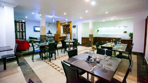 A restaurant with multiple dining tables and chairs, a TV mounted on the wall, and a counter area. - GENESIS COTTAGE (Port Harcourt)