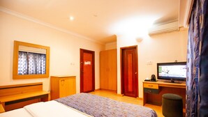 A hotel room with a bed, a desk with a computer, a television, and a window with curtains. - GENESIS COTTAGE (Port Harcourt)