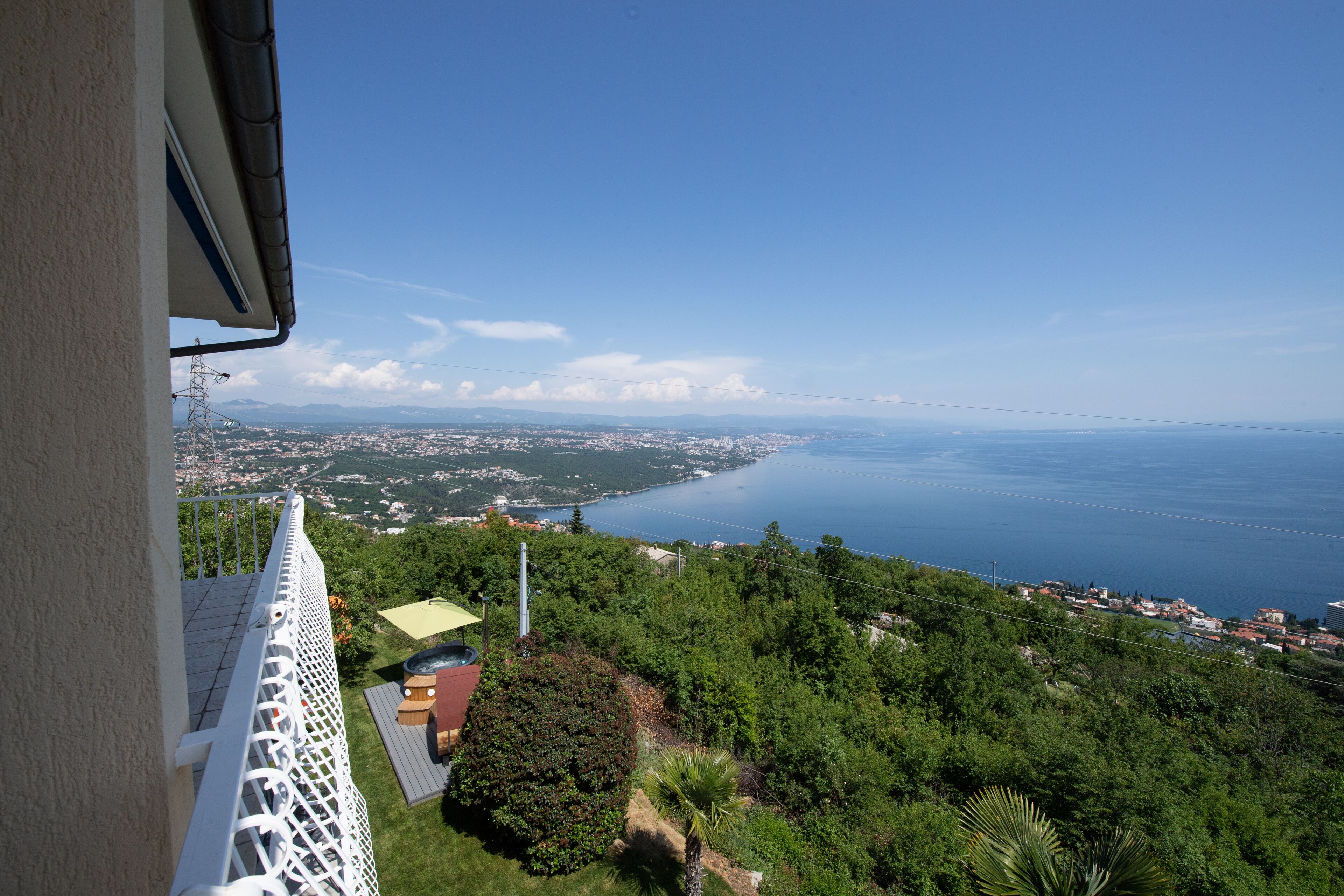 A balcony with a view of a coastal town, greenery, and a clear sky.