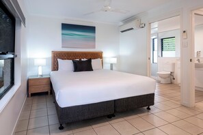 Camera d'albergo con un letto grande, due comodini, una ventola a soffitto, una finestra e un bagno visibile attraverso una porta aperta.