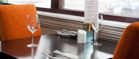 Una mesa de comedor con un menú, un salero y un posavasos, y una copa de vino.