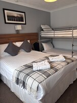A hotel room with a large bed, a bunk bed, a framed picture on the wall, and a lamp.