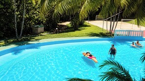 A swimming pool with clear blue water, surrounded by greenery and a fenced area.