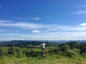 Eine Person steht auf einem Felsen mit Blick auf eine grüne Landschaft und Hügel in der Ferne.