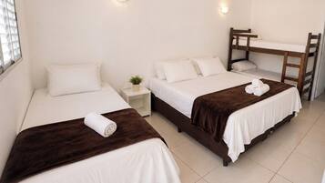 A hotel room with two single beds, a small bedside table with a plant, a desk with a chair, and a ceiling fan.