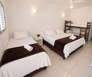 A hotel room with two single beds, a small bedside table with a plant, a desk with a chair, and a ceiling fan.