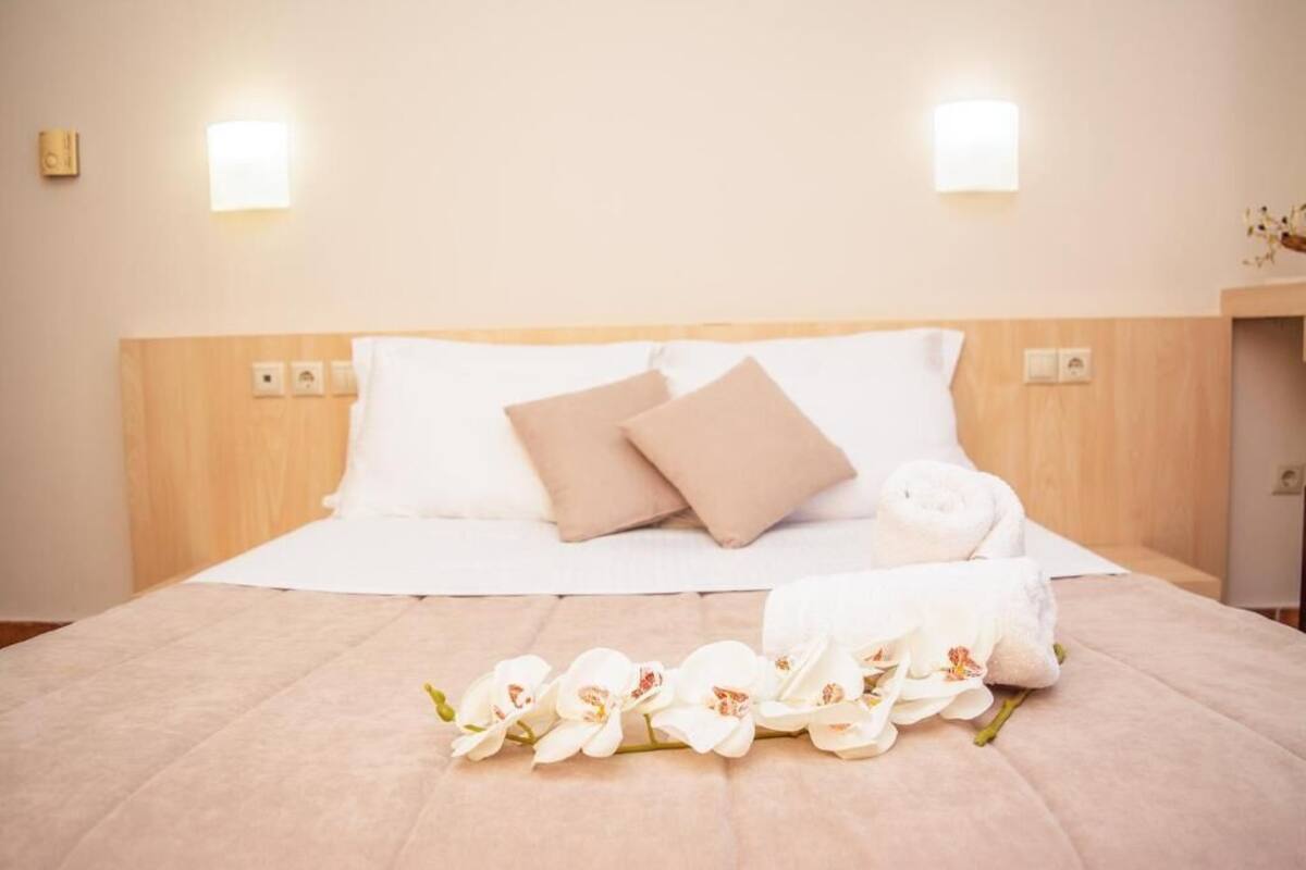 A neatly made bed with white and beige pillows, a rolled towel, and white orchids on the bed.
