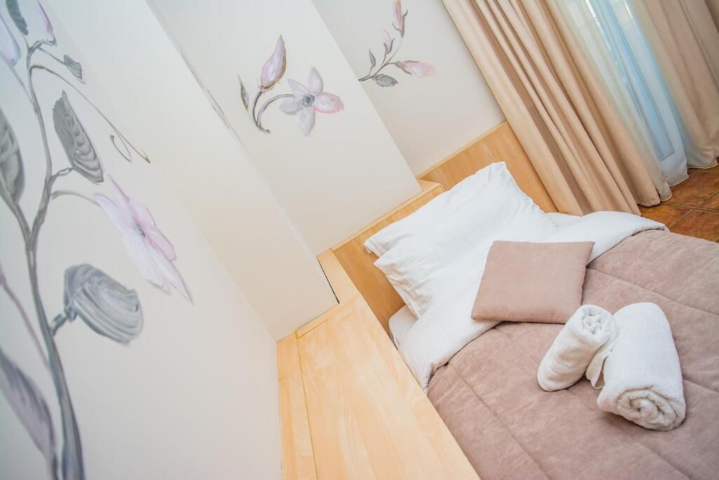 A neatly made bed with white and pink pillows, a rolled white towel, and floral wall art.