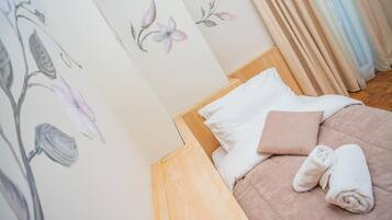 A neatly made bed with white and pink pillows, a rolled white towel, and floral wall art.