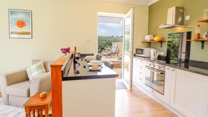 A modern kitchen with a central island, white cabinetry, and a view to an outdoor patio. - Cam O'r Fechan Annexe (Llangollen)