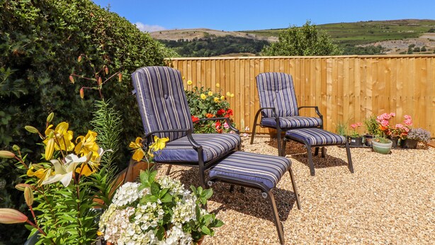 Two striped lounge chairs with cushions, a wooden fence, and a variety of potted plants and flowers. - Cam O'r Fechan Annexe (Llangollen)