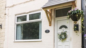 A white cottage with a large window, a door with a number plate, and a hanging flower basket.