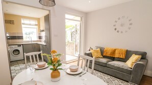 A dining area with a round table set for four, a grey sofa with yellow cushions, and a wall clock.
