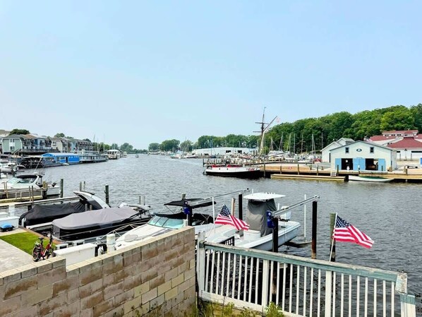 A marina with boats docked, a small docked boat with an American flag, and a building with a red roof in the background.