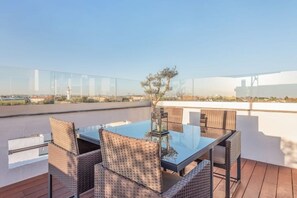 A rooftop terrace with a glass table and wicker chairs, offering a clear view of the cityscape. - Rooftop Pied-à-terre private Sauna & Jacuzzi by BentoBox. (LISBON)