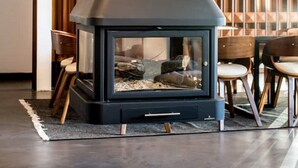 A modern living room with a black wood-burning stove, wooden paneling on the walls, and a dining area with chairs and a table. - Bento Box Vintage Family Villa & Hot Pool (Vilamoura)