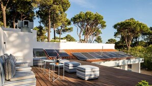 An outdoor deck with solar panels, a seating area with striped cushions, and a pool. - Bento Box Vintage Family Villa & Hot Pool (Vilamoura)
