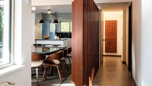 A modern interior with a wooden ceiling, a kitchen area with a dining table, and a hallway leading to a door. - Bento Box Vintage Family Villa & Hot Pool (Vilamoura)