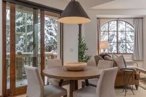 Relax in this inviting living area with a round table, comfortable seating, and a sofa, perfect for unwinding with a view of snow-covered trees.
