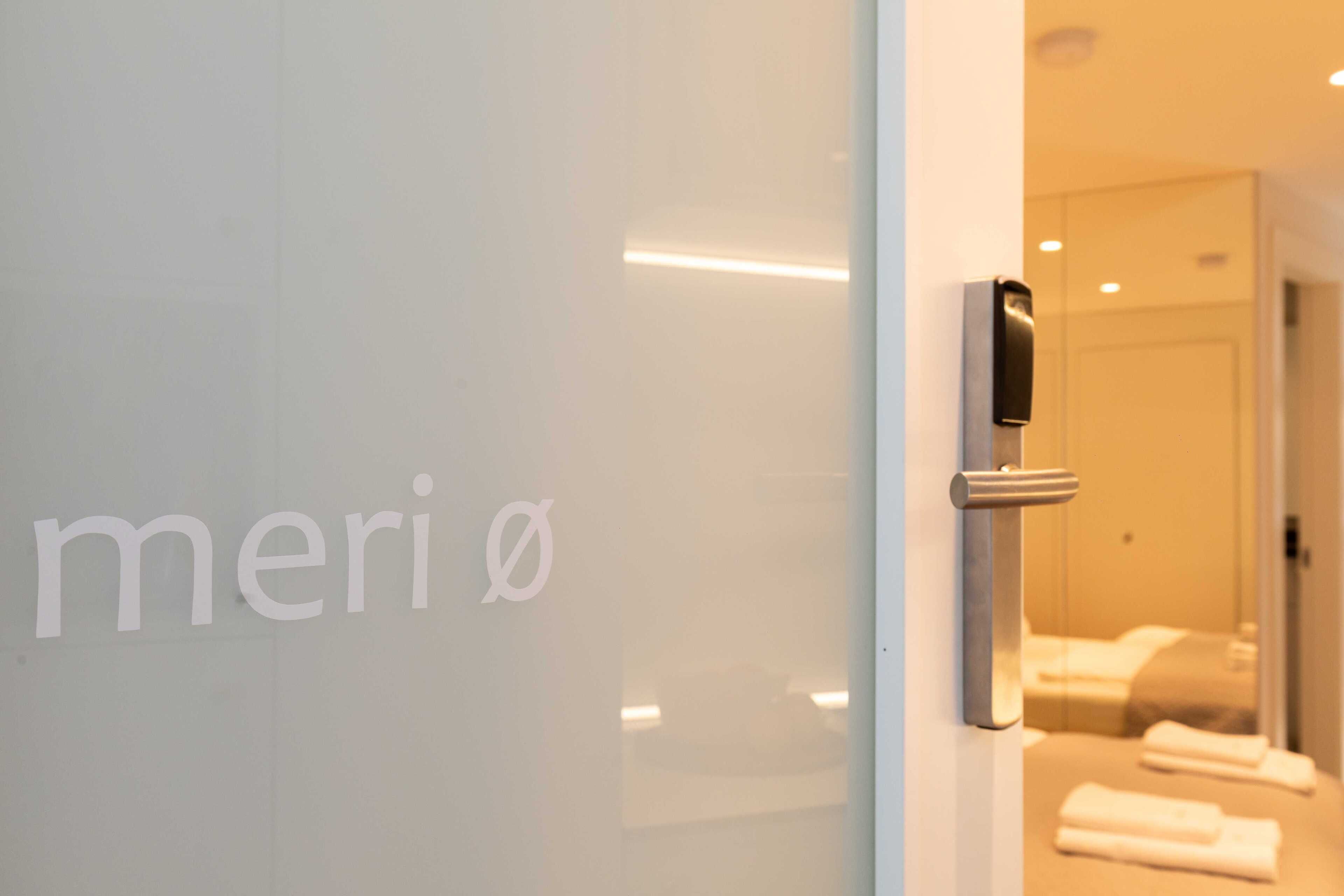Quarto de hotel com parede de vidro, porta com puxador e cama com toalhas.