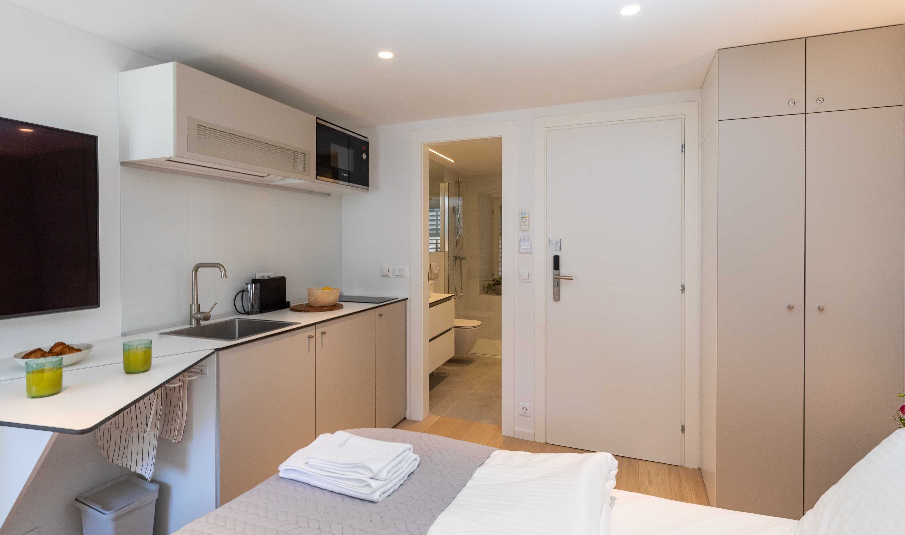 A compact hotel room with a kitchenette, a bed, and a wardrobe.