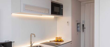 Una cocina moderna con microondas integrado, pileta de acero inoxidable y tabla de madera con limones.