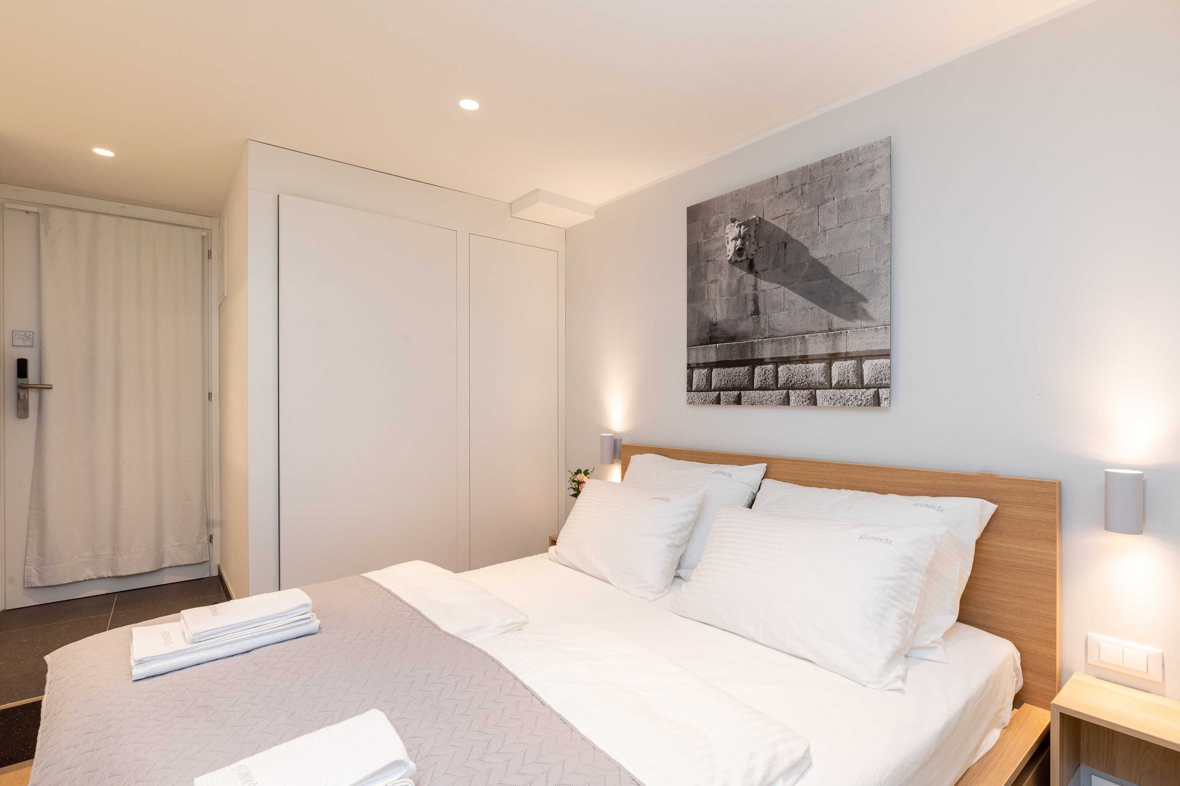 A neatly made bed with white linens, a wooden headboard, and a wall-mounted artwork above it.