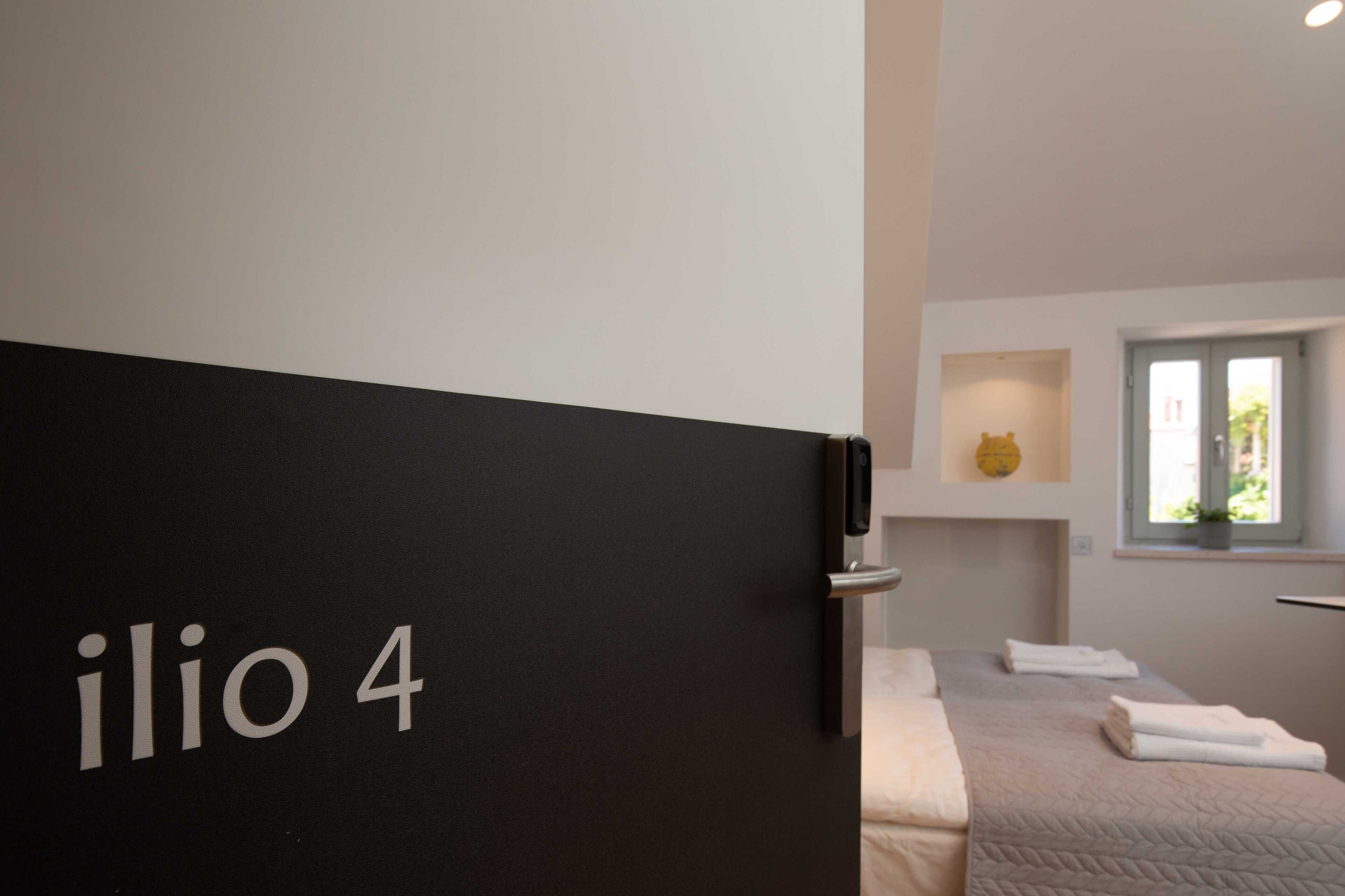 Moderni hotellihuone, jonka mustassa ovessa on kyltti, jossa lukee ”ilio 4”.