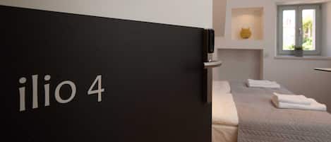 A modern hotel room with a black door labeled "ilio 4".